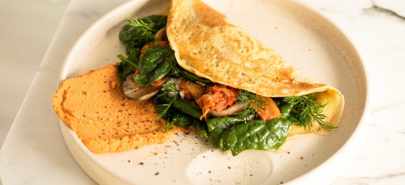 omelette in a plate with some spinach and sauce